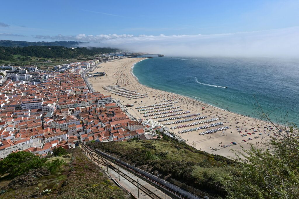 Aerial view of Nazaré on the Silver Coast showing the curved sandy beach, Atlantic Ocean, and town of white buildings with terracotta rooftops — UK to Portugal removals to the Silver Coast by Trunk Logistics