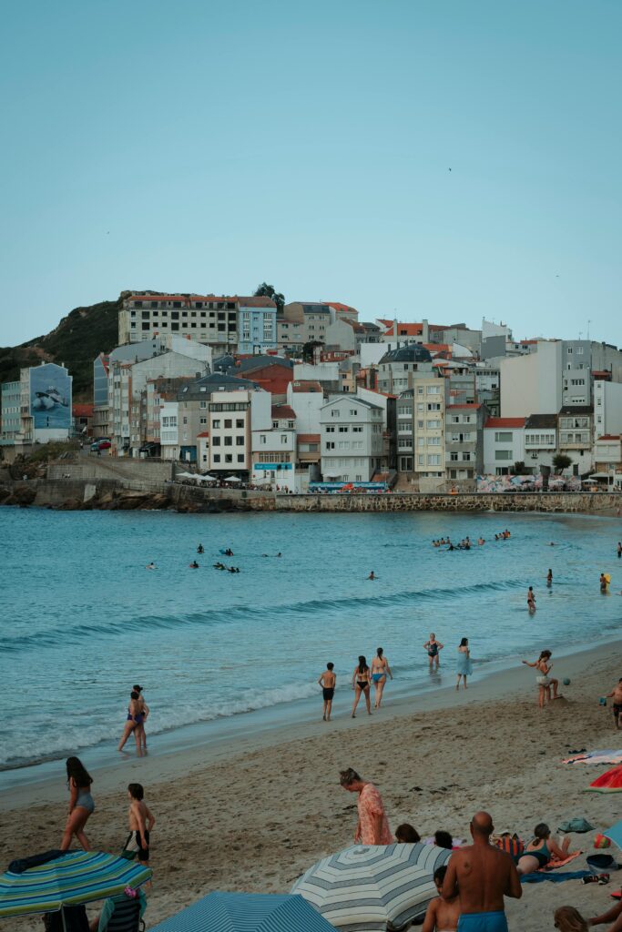 Busy beach in front of a Spanish coastal town with hillside buildings — UK to Spain removals to Costa regions and coastal Spanish addresses by Trunk Logistics
