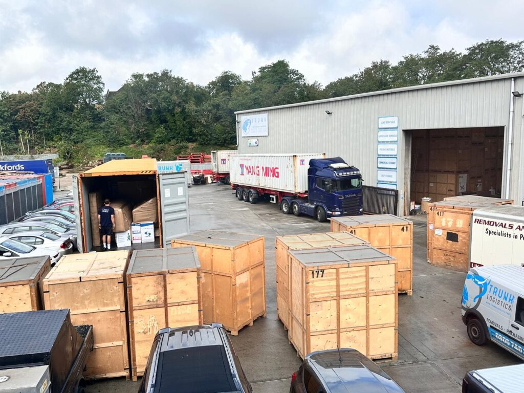 Trunk Logistics Essex depot with shipping containers, wooden storage crates, and removal vehicles being loaded for international shipping to New Zealand