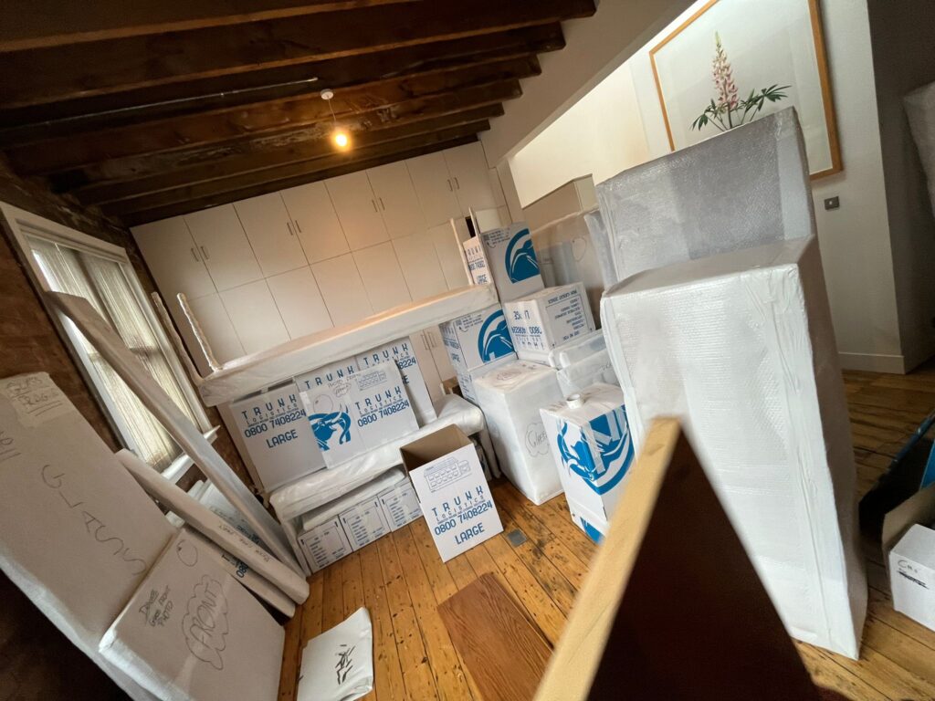 Trunk Logistics export packing in progress — branded removal boxes, bubble-wrapped furniture, and protected artwork staged in a client property ready for international shipping