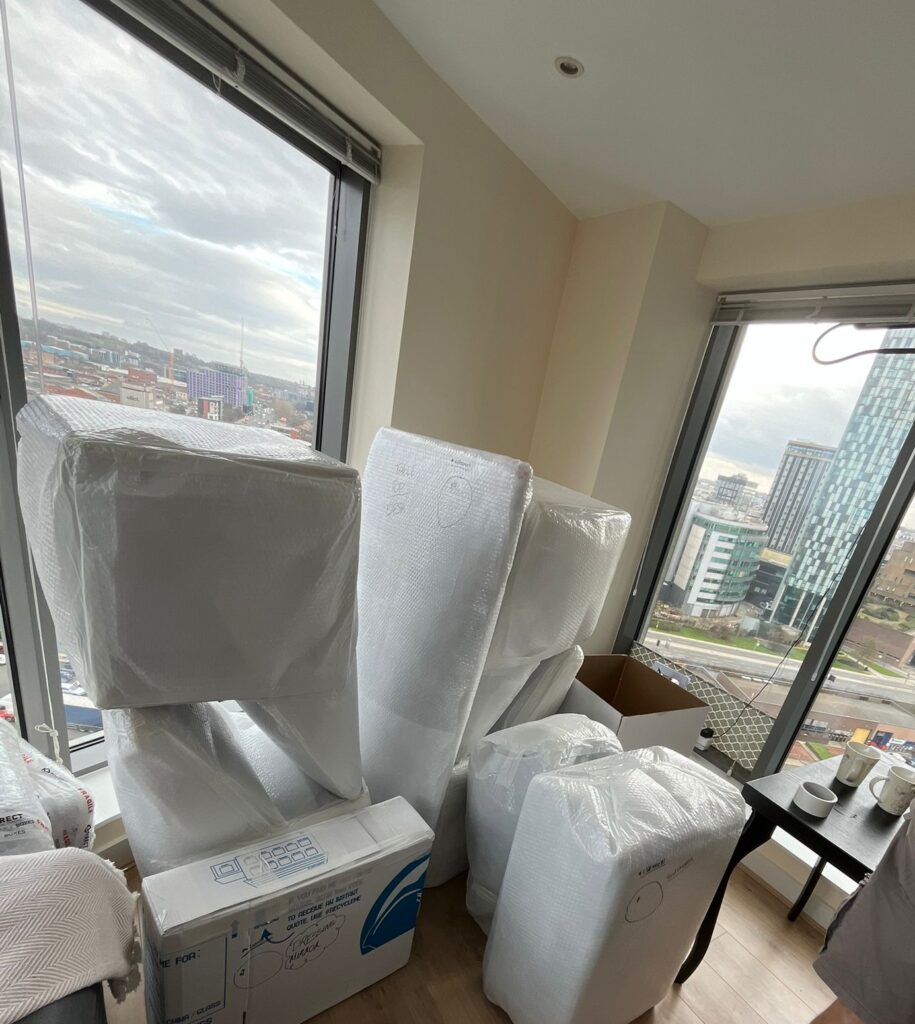 Trunk Logistics crew member alongside bubble-wrapped chairs and export cartons in a high-rise apartment prepared for international removal — export packing service for overseas shipping