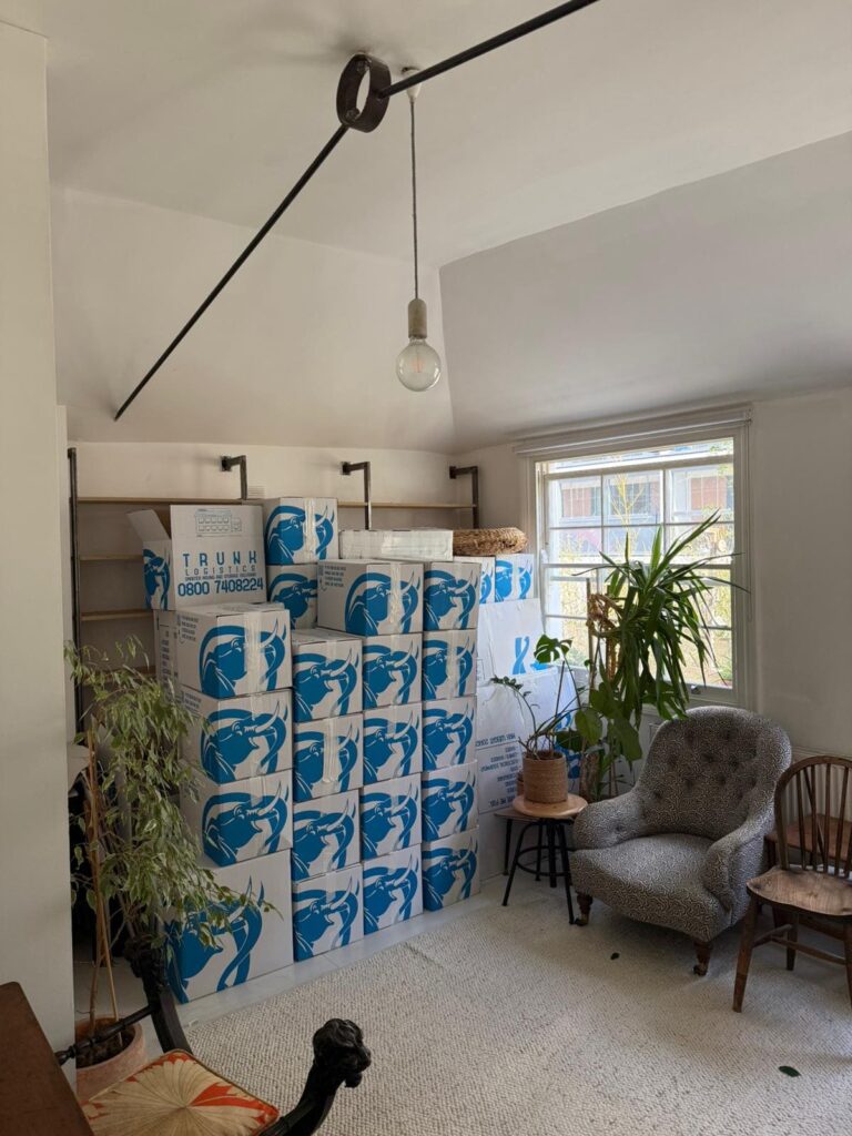Stack of Trunk Logistics branded removal boxes packed and ready in a residential living room before moving day — professional packing service for home removals