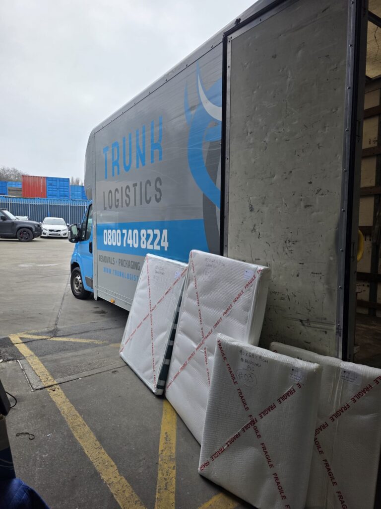 Trunk Logistics removal van parked at depot with fragile-labelled bubble-wrapped export items staged for container loading — international removal export packing service