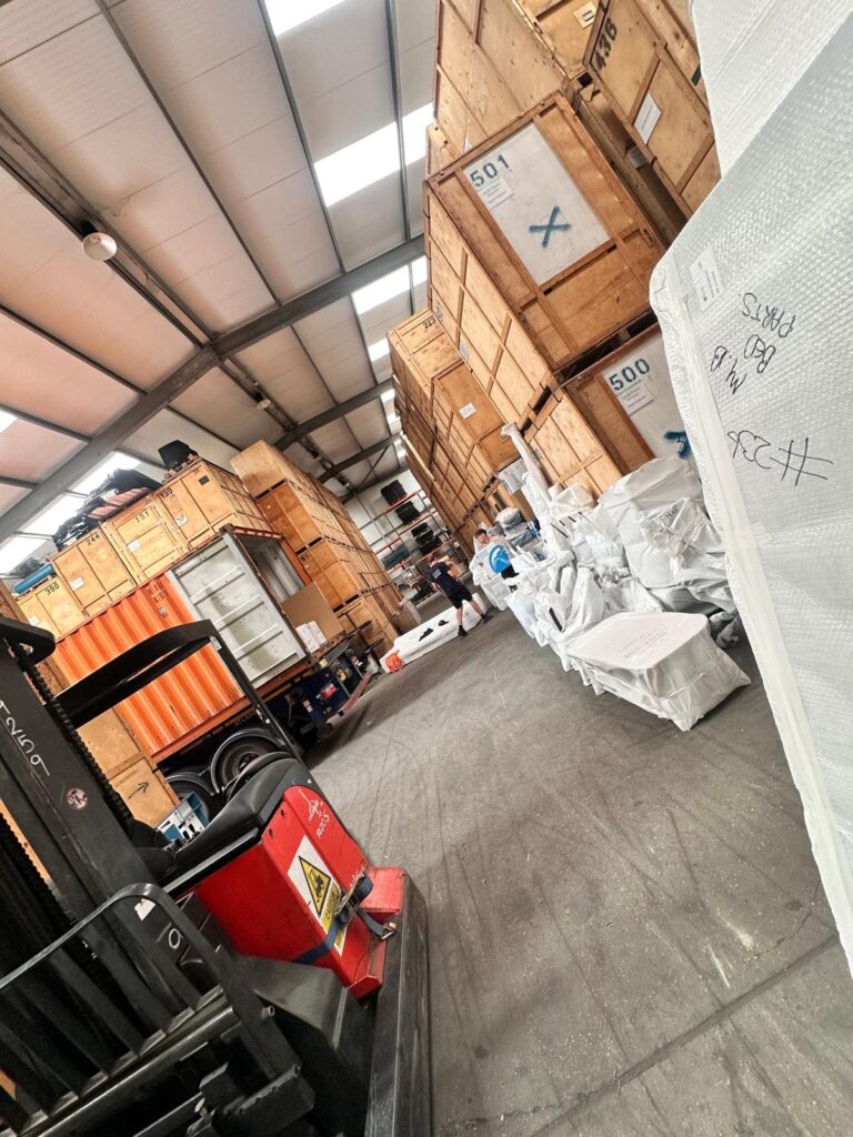 Trunk Logistics Essex warehouse interior showing numbered wooden storage crates, export-wrapped furniture, and shipping containers being prepared for UK to Canada international removals