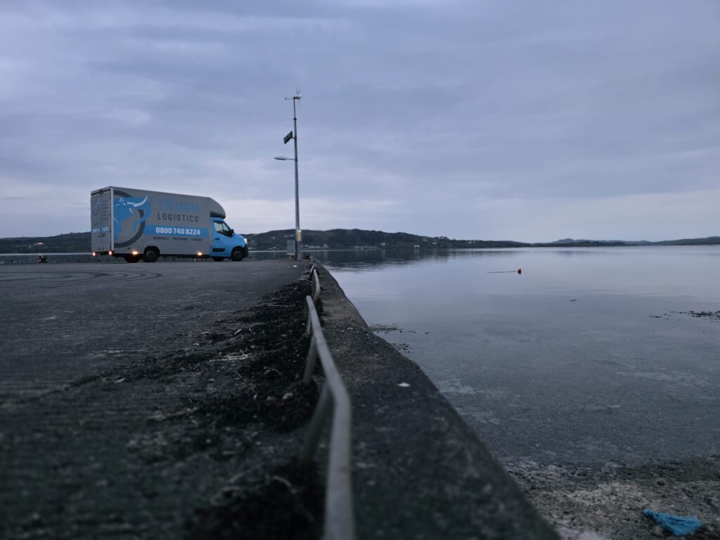 Trunk Logistics removal van on a pier at dawn in Kerrykeel, County Donegal, with calm lough water in the foreground