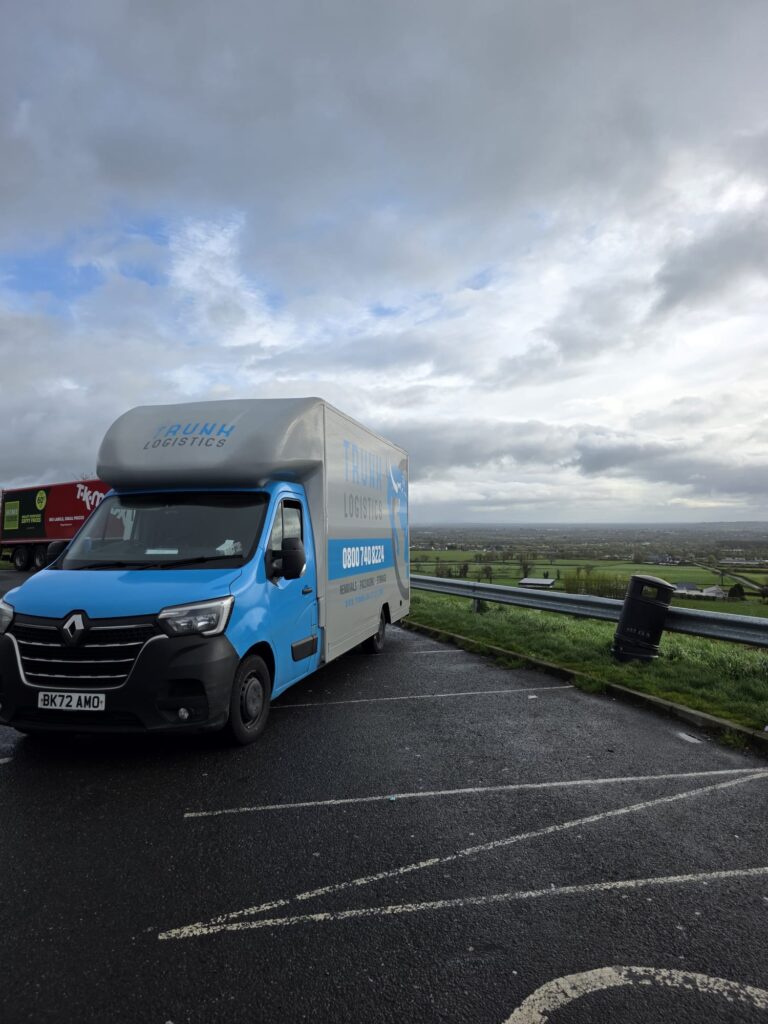 Trunk Logistics removal van at a County Wicklow viewpoint with green Irish countryside and dramatic sky — Ireland to UK removal service