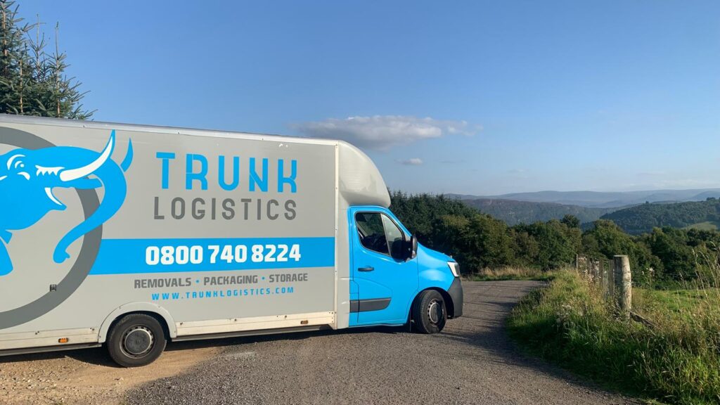 Trunk Logistics removal van on a rural Irish road with a wooded valley and hillside in the background — Ireland to UK removal service