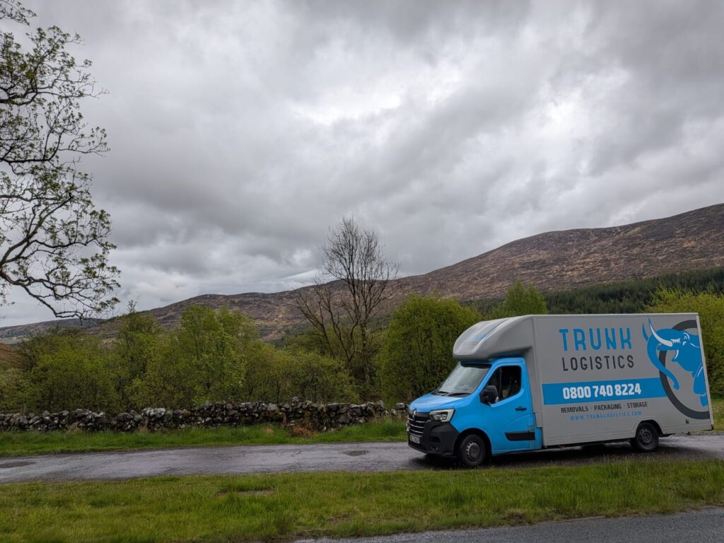 Trunk Logistics removal van on a rural mountain road with green valley and hills in the background — Ireland to UK removal service